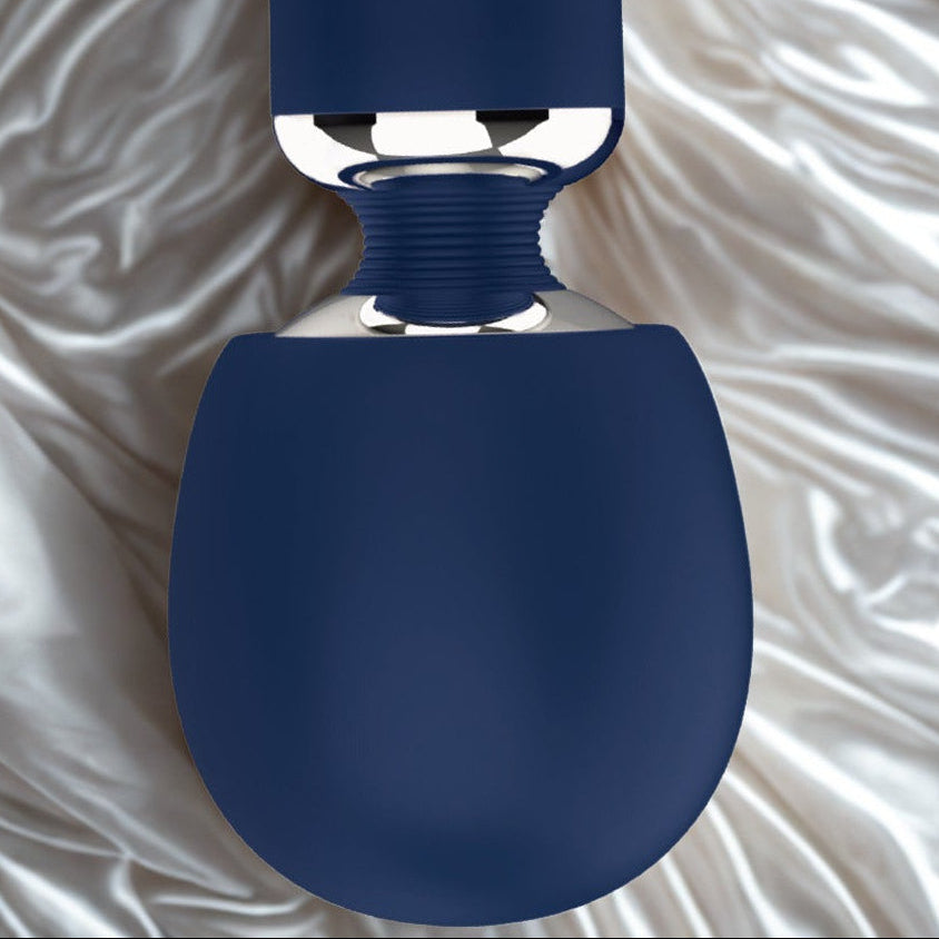 A close-up image of the Give In To Me massager, inverted to show the flexible percussive head, and the flexible adaptive neck on white and gold silk sheets. 
