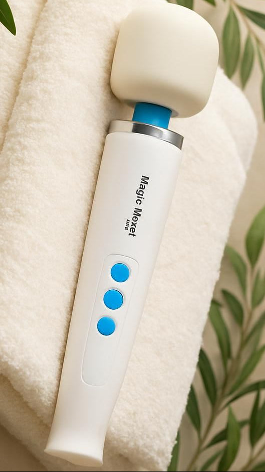 A close-up of a white Magic Wand Mini wellness device resting on a stack of plush, cream-colored towels. Framed by soft eucalyptus leaves, this scene visualizes an easy grip, gender neutral inclusivity and Simple Elegance. The clean, spa-like environment emphasizes Medical-Grade silicone and Adaptive Sensory Comfort.
