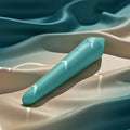 A matte turquoise blue compact wellness device on luxury, rippling silk showing waterproof design and sensory focus.