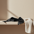 Adaptive intimacy sashes in black silk folded on a travertine stone shelf for sensory wellness.