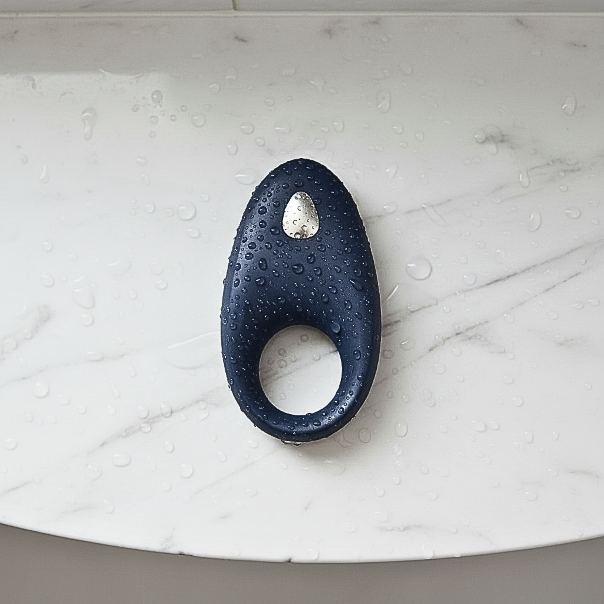 App-controlled constriction ring in blue silicone on a marble shower shelf with water droplets for a waterproof design.