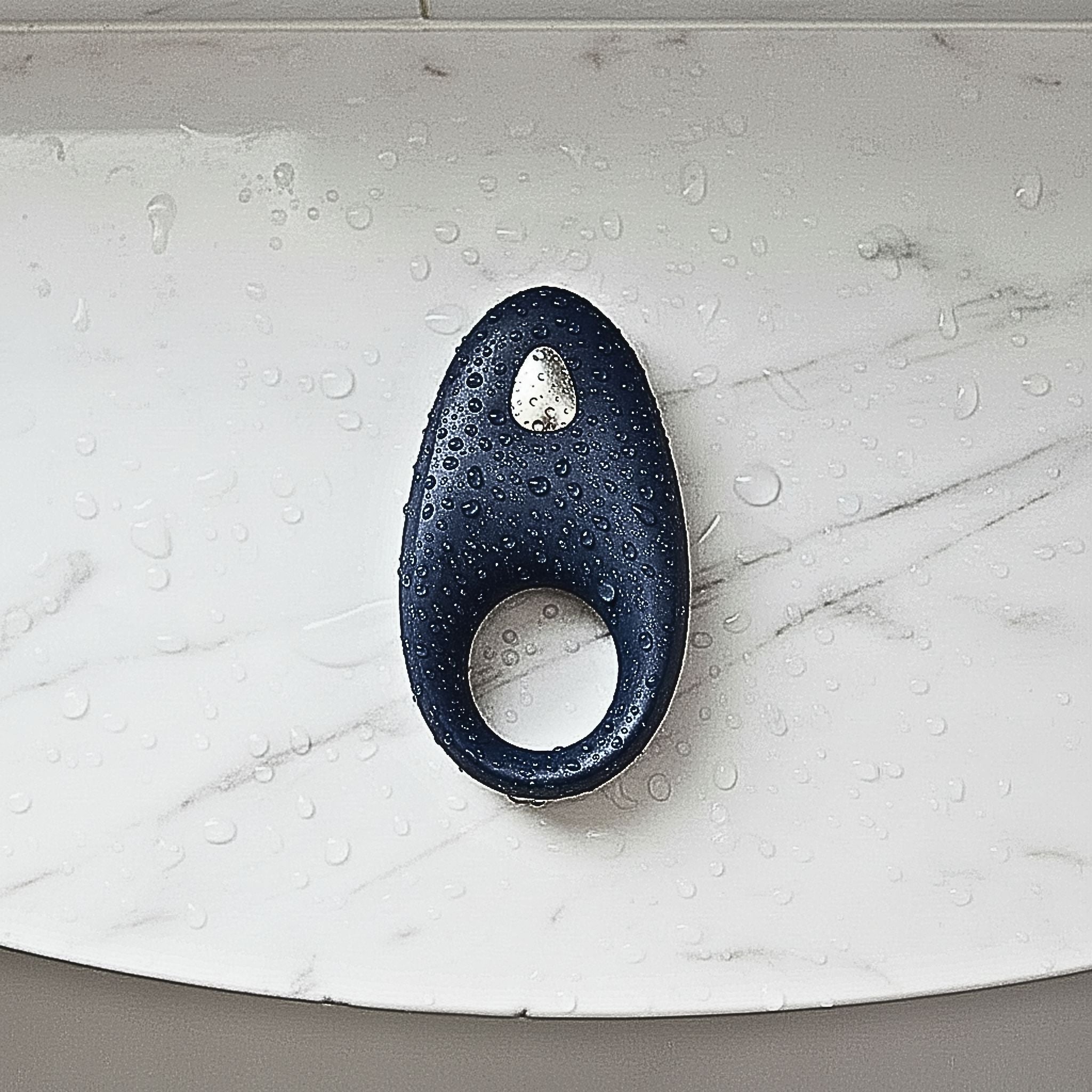 App-controlled constriction ring in blue silicone on a shelf with water droplets for a waterproof design.