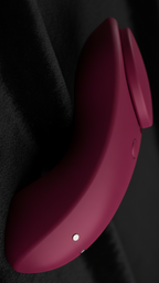 Cloe-up of a deep berry-red, ergonomically curved wellness device resting on plush black velvet. Cool, diffused lighting highlights the matte silicone texture and the silver magnetic contact points, emphasizing Discreet Sensory Pulse technology and high-end design.