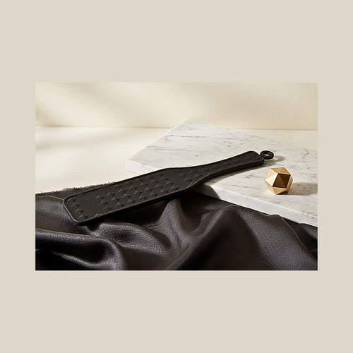 Matte black silicone sensory paddle with diamond texture on white marble for tactile sensory contrast.
