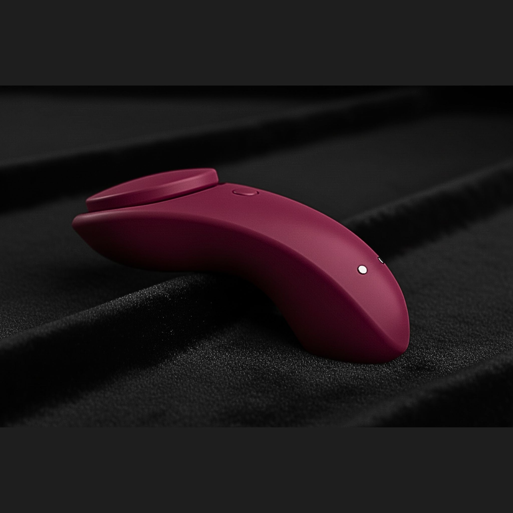 Red app controlled massager resting on luxury black felt used for neuro-inclusive sensory.