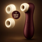 Satisfyer Pro 2 Generation 3 liquid air stimulator in wine red, standing upright against a warmly lit, dark background. Two extra white silicone replacement caps float to the left, along with a circular badge reading plus new cap.