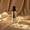 Sliquid unscented massage oil rests on warm gold silk with white petals for intimate wellness.
