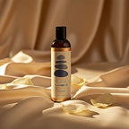 Sliquid unscented massage oil rests on warm gold silk with white petals for intimate wellness.